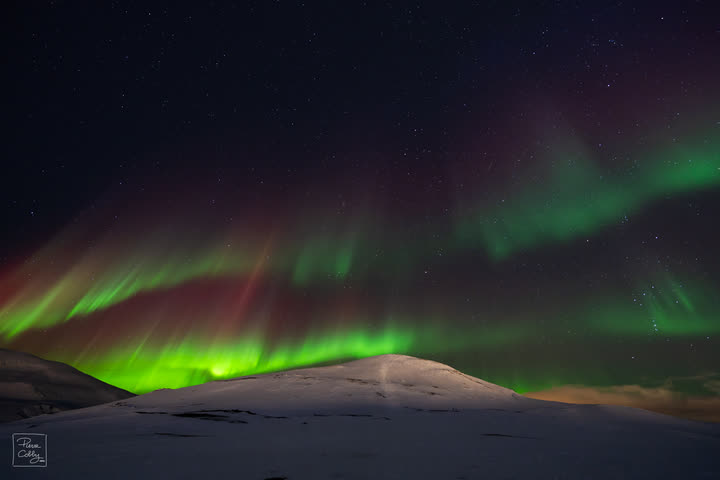 Bright green aurora curtain over snow-covered mountains