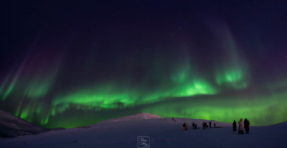 Panorama of the northern lights with silhouettes of people on the snow