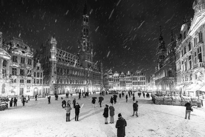 Snow-covered Grand-Place with people walking at night, in black and white