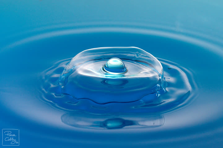 Water drop forming a dome on a blue surface