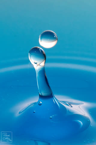 Two water drops colliding above a blue splash