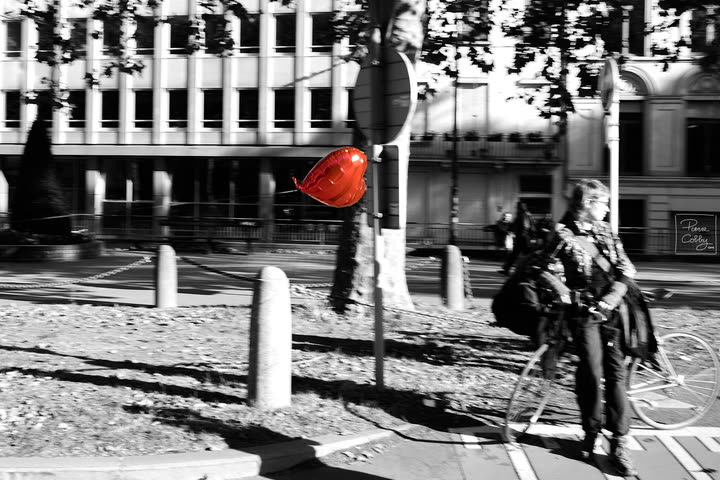 Red heart-shaped balloon floating past a cyclist in a black and white street scene
